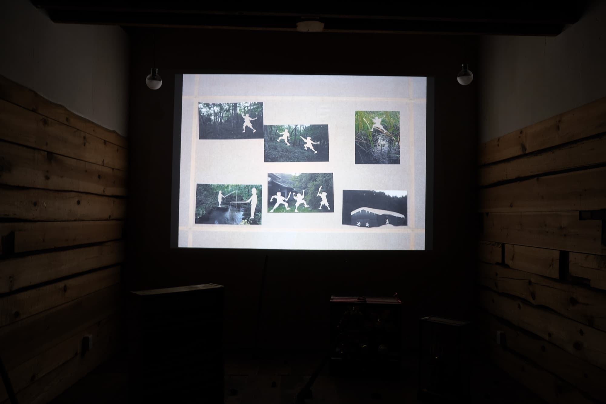 スクリーンに、風景写真と影絵人形を重ねた画面が映っている
